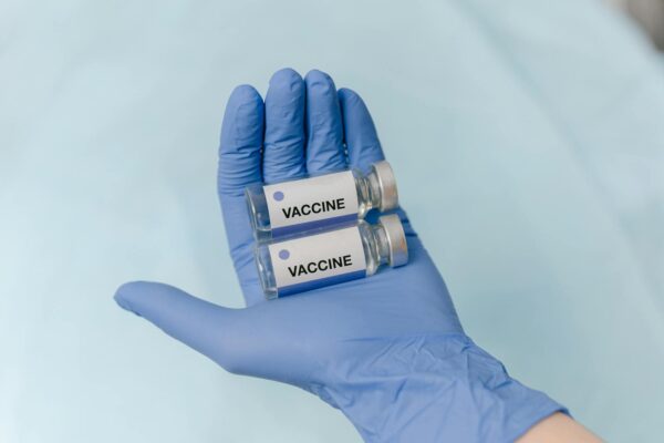 Two vaccine vials held securely in a latex-gloved hand, against a neutral background.